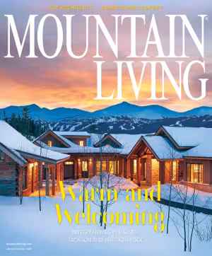 Snowy cabin at sunset with glowing windows and mountain backdrop. Magazine cover photograph.