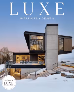 Modern house in snowy landscape at dusk, with warm interior lights. Magazine cover.