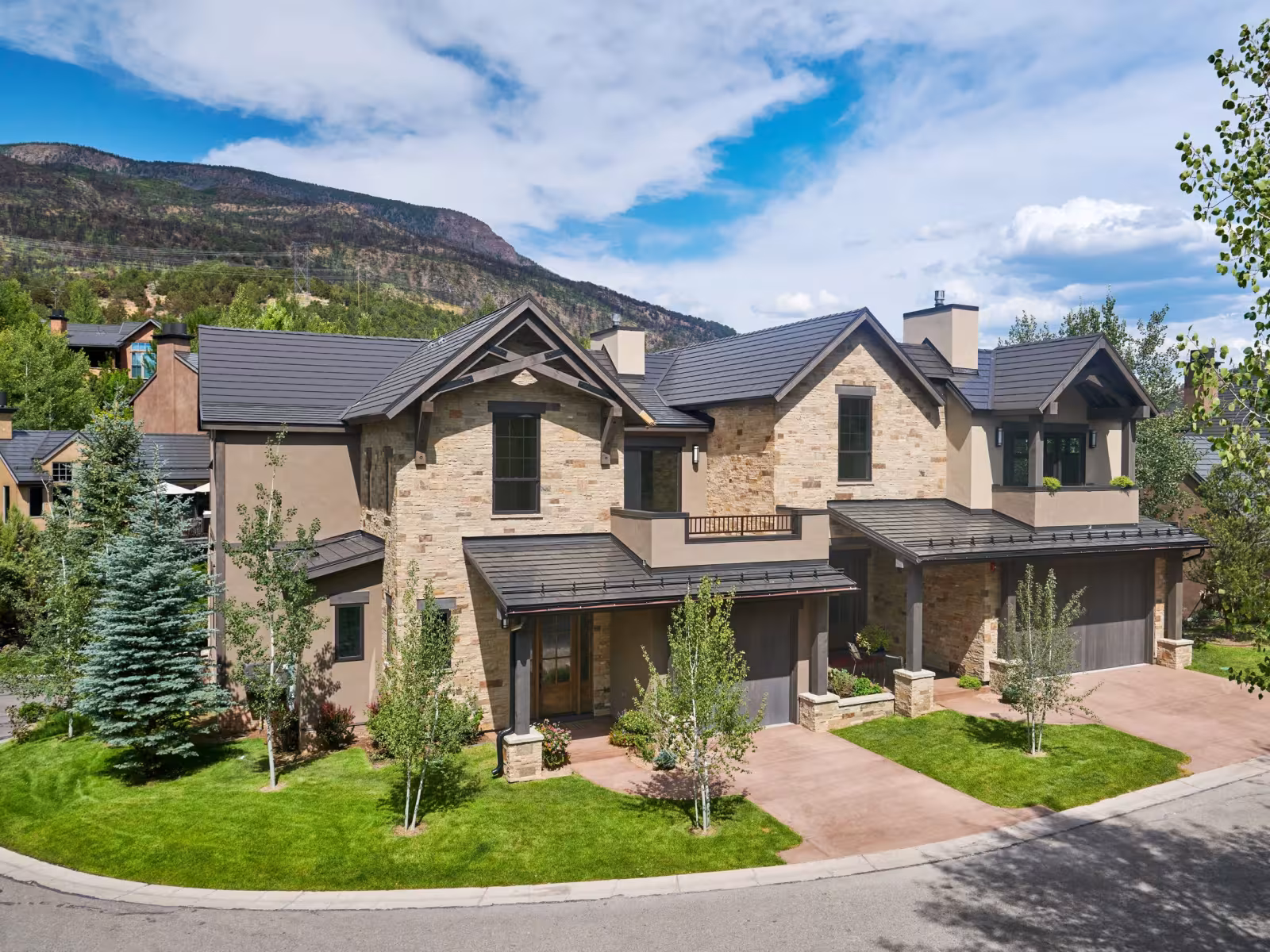 Stone and wood house with manicured garden, mountain and blue sky in background.