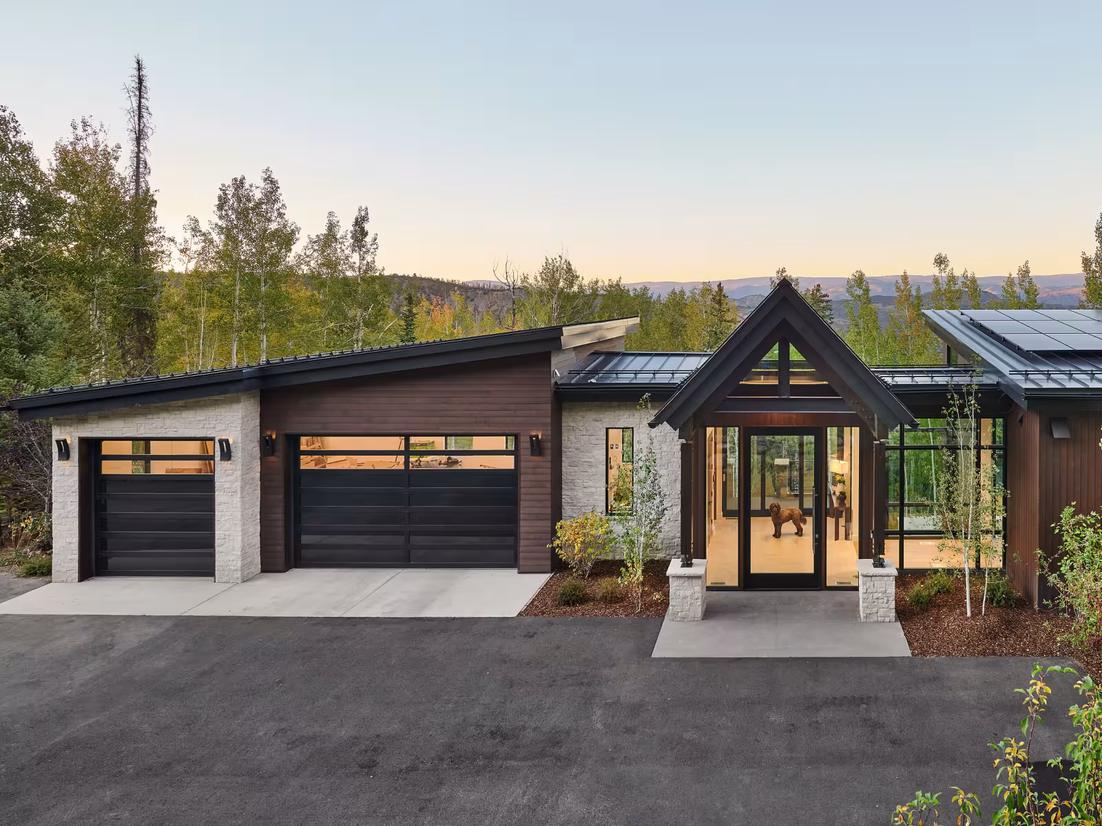 Modern house with large windows and driveway, set among trees.