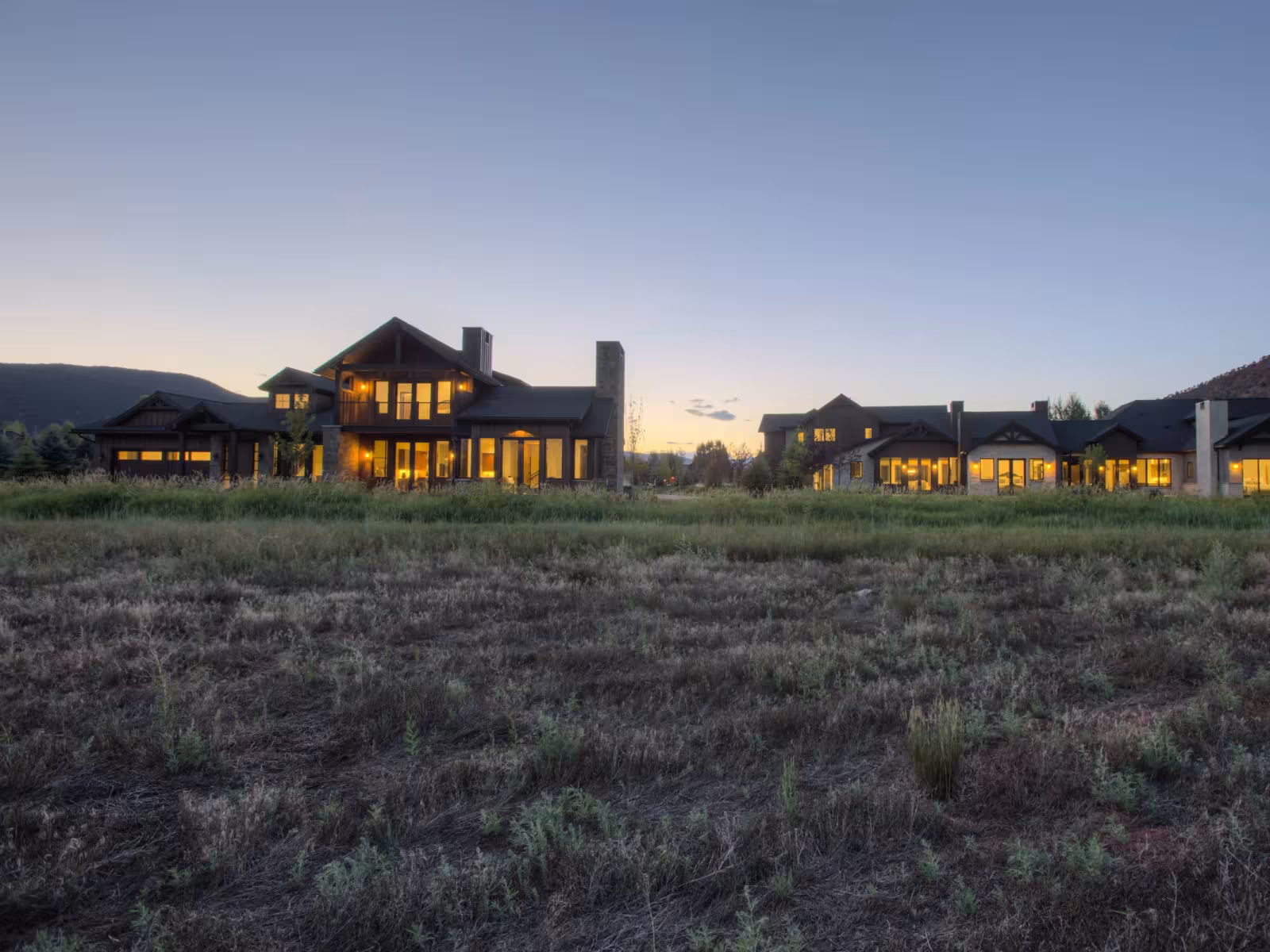 Luxurious house with lit windows at dusk, surrounded by grassland.