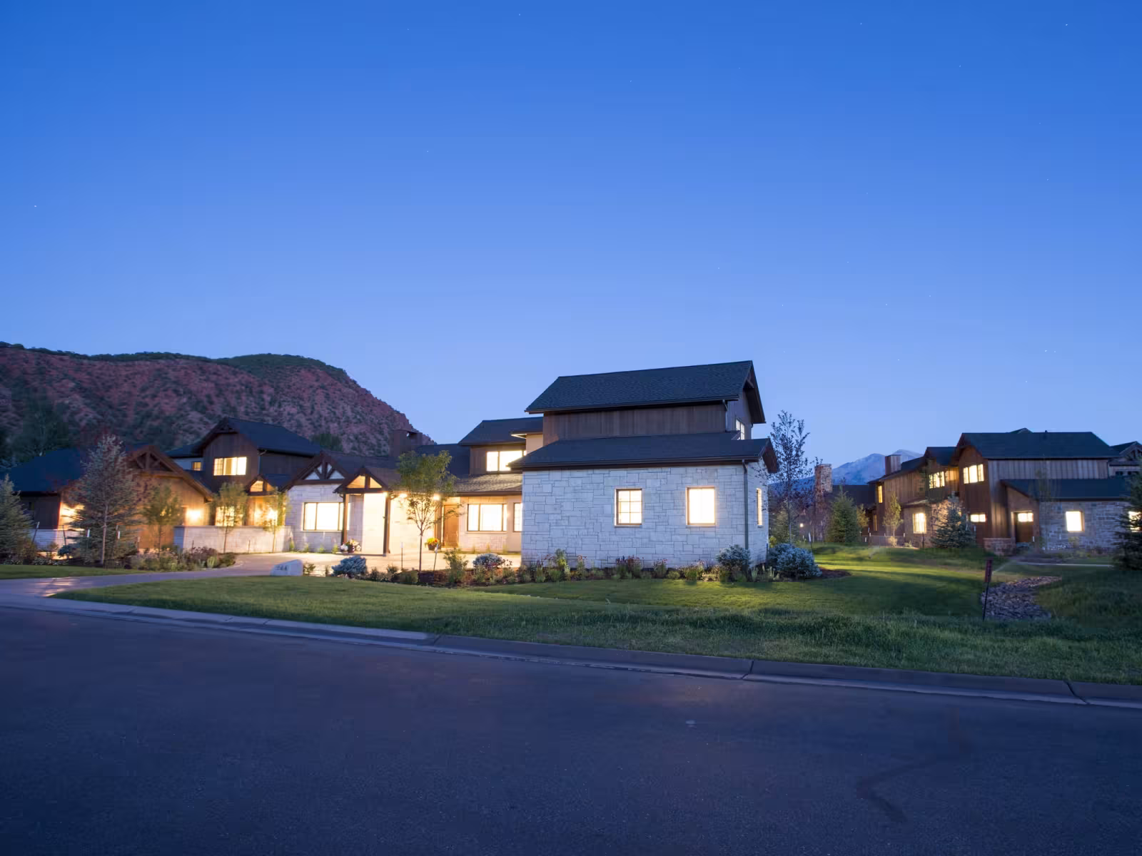 Houses with lit windows at dusk, mountains in the background.