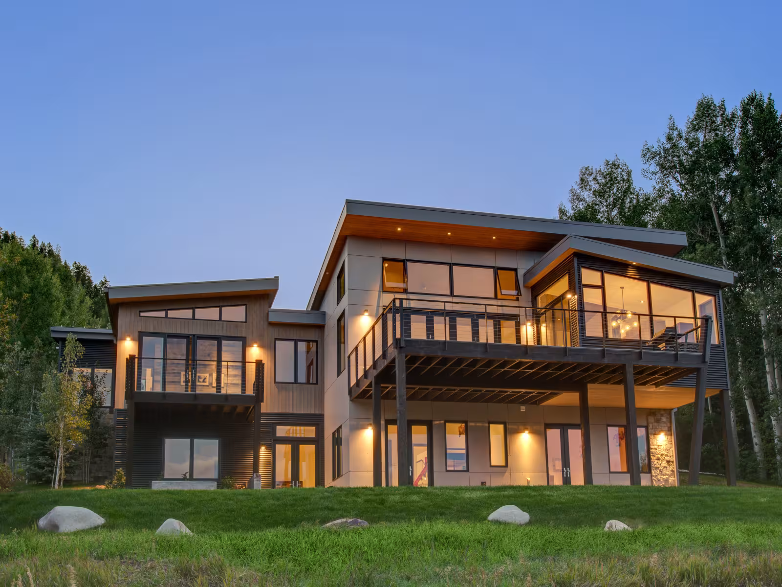 Modern house with large windows, illuminated at dusk, surrounded by trees.