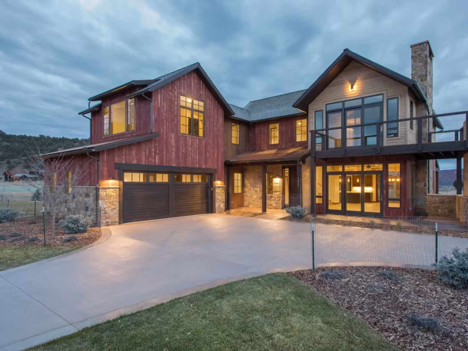 Spacious modern house at dusk with glowing windows and a large driveway.