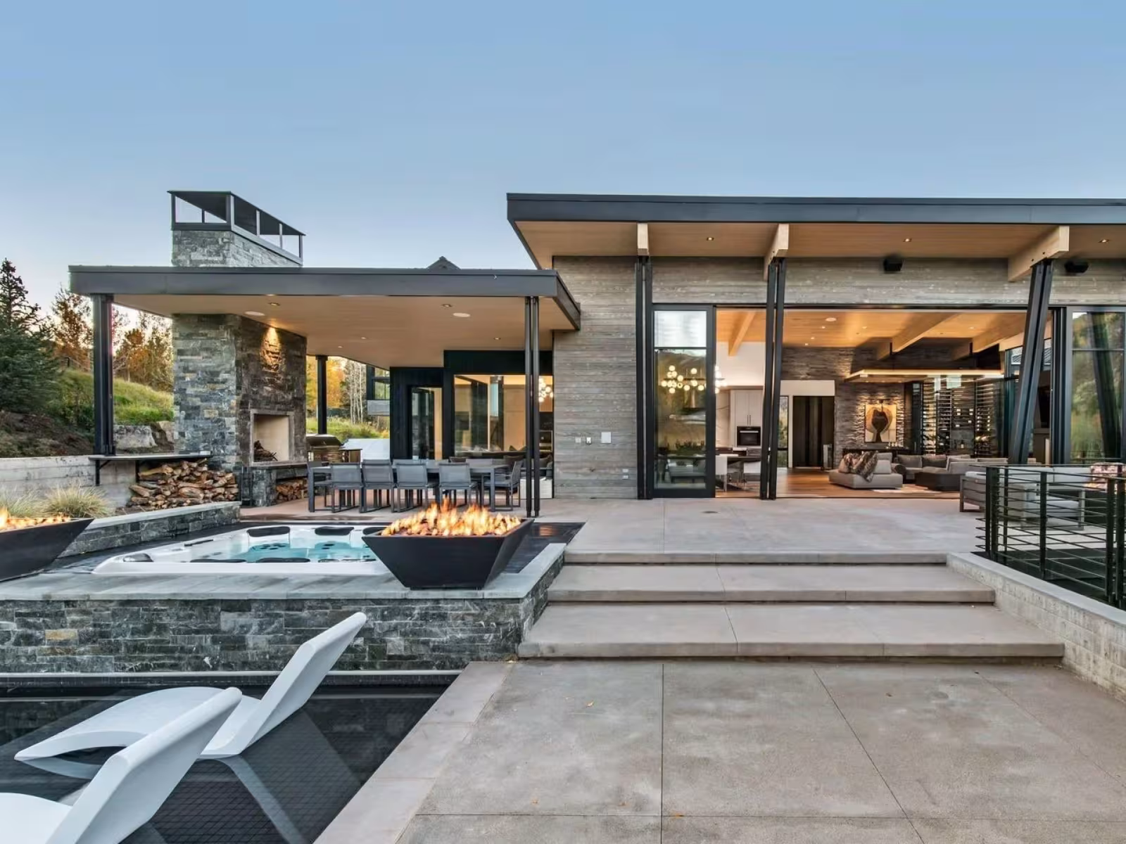 Modern house with pool, fire pit, and large patio at sunset.