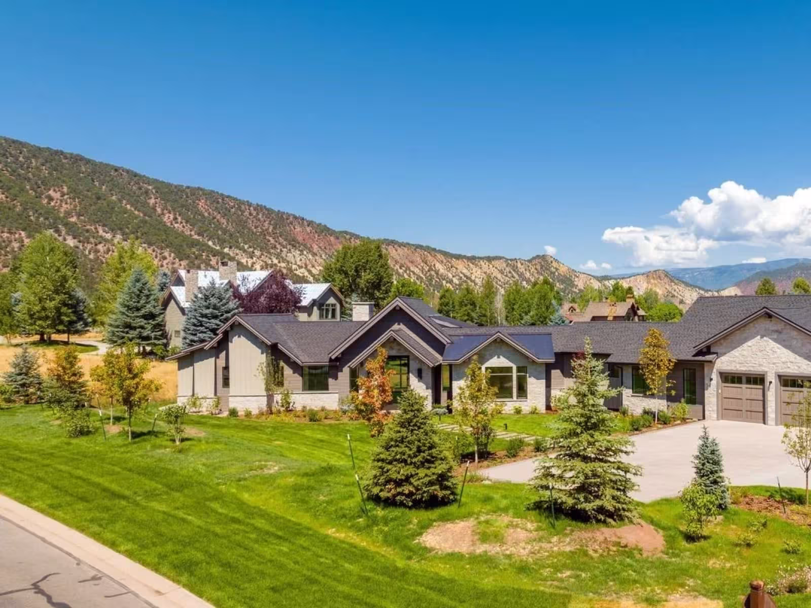 Elegant house with manicured lawn, mountain backdrop, under clear blue sky.