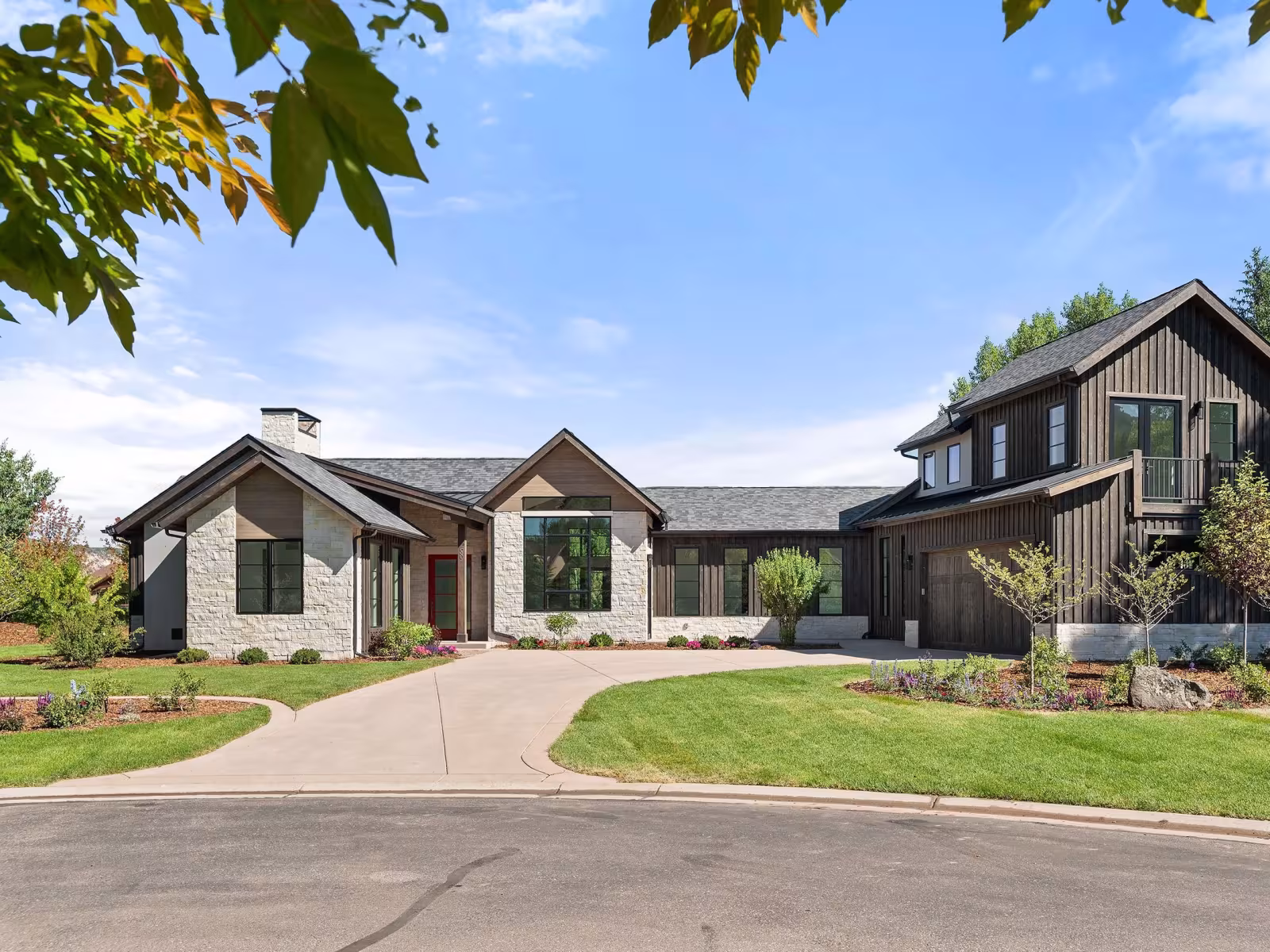 Modern house with large windows, grey exterior, and a curved driveway, surrounded by greenery.