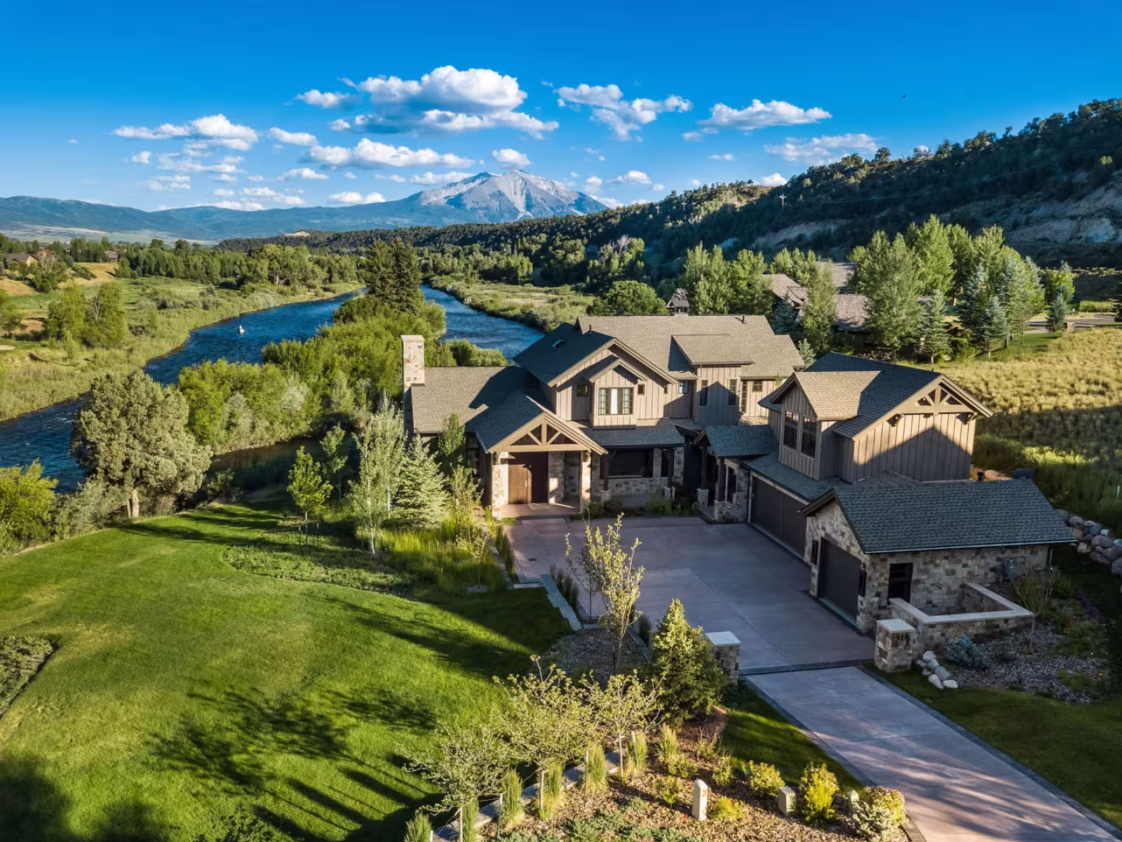 Large countryside house beside a river, surrounded by greenery and mountains.