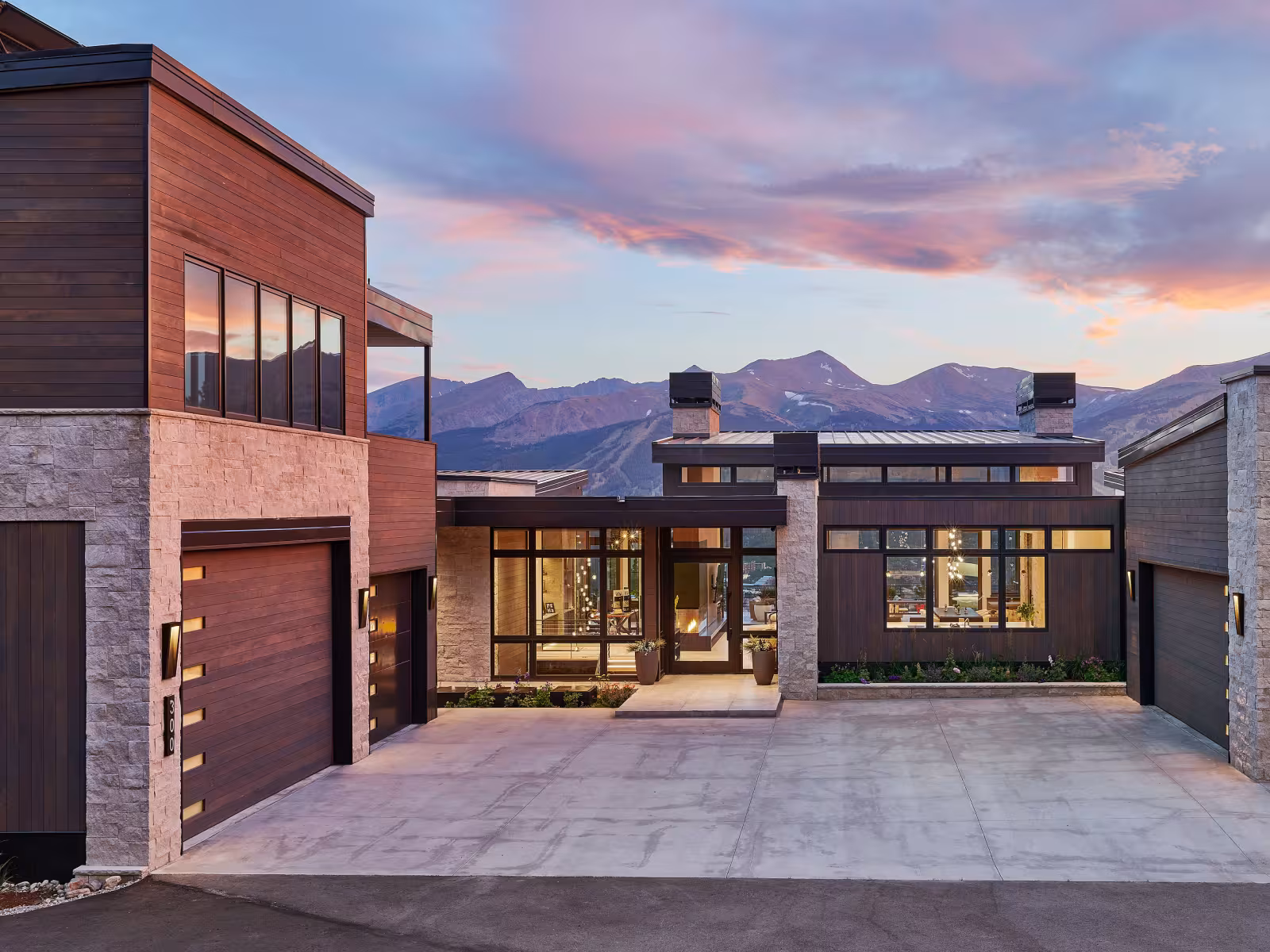 Modern house with large windows and mountain backdrop at sunset.