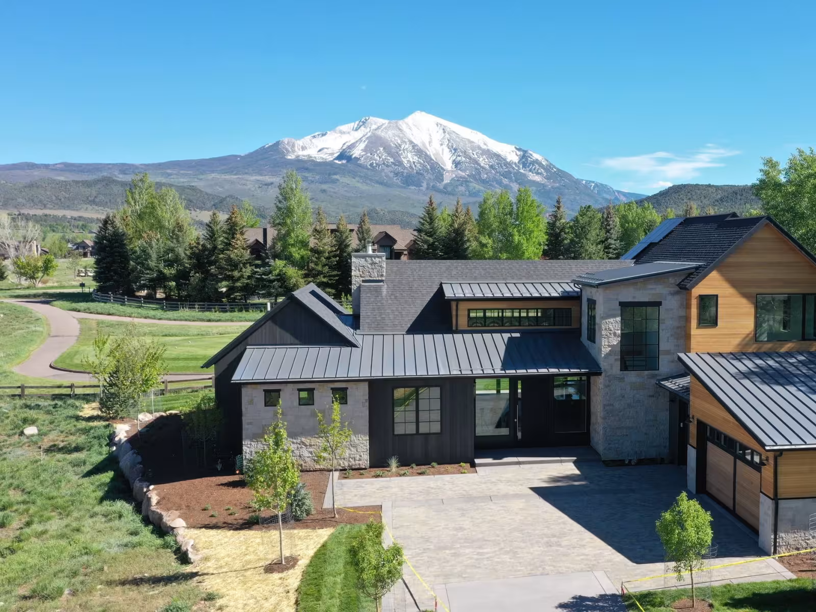 Modern house with grey roof, mountain and trees in the background.