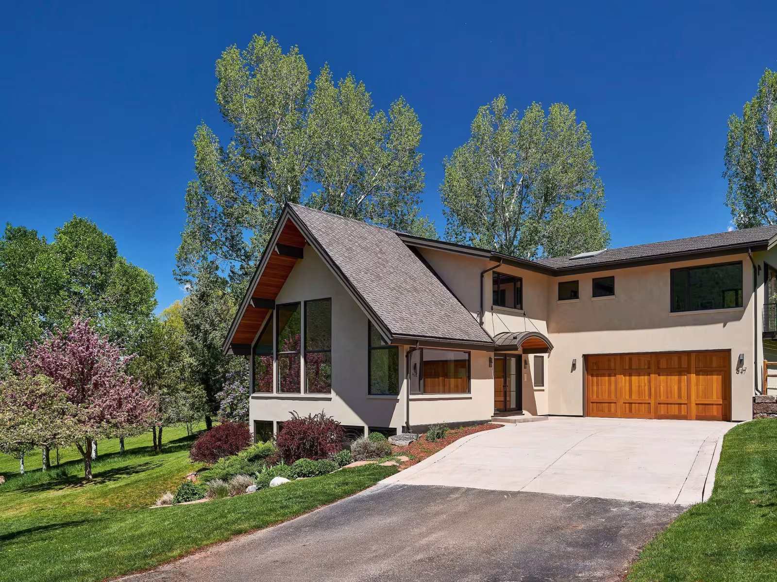 Modern house with large windows, surrounded by lush trees and a well-kept lawn.