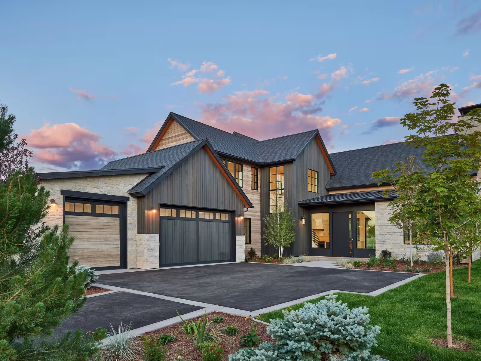 Modern house with large garage, neat driveway, and trees, set against a vibrant evening sky.