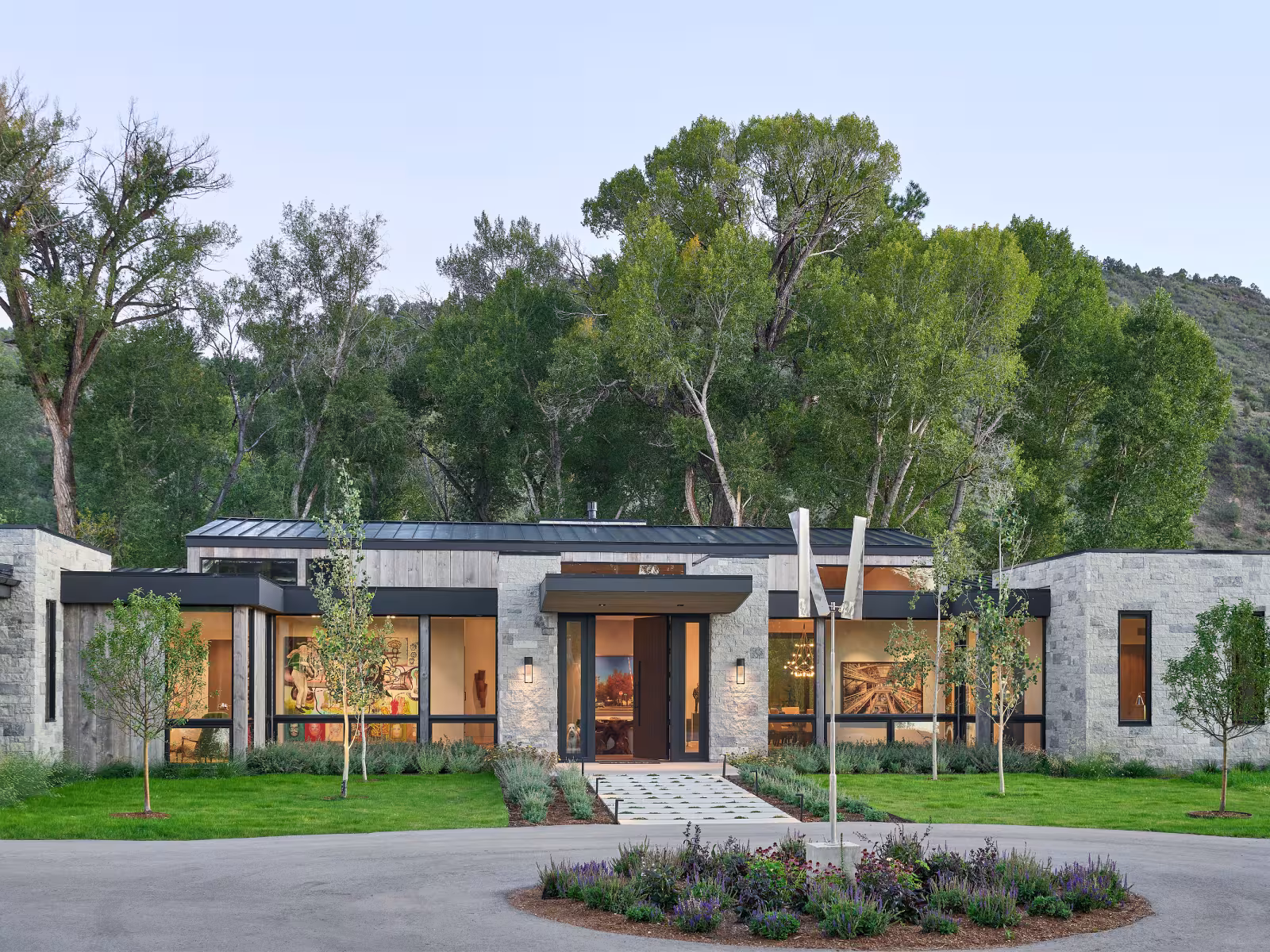 Modern house with large windows, surrounded by trees and a garden.