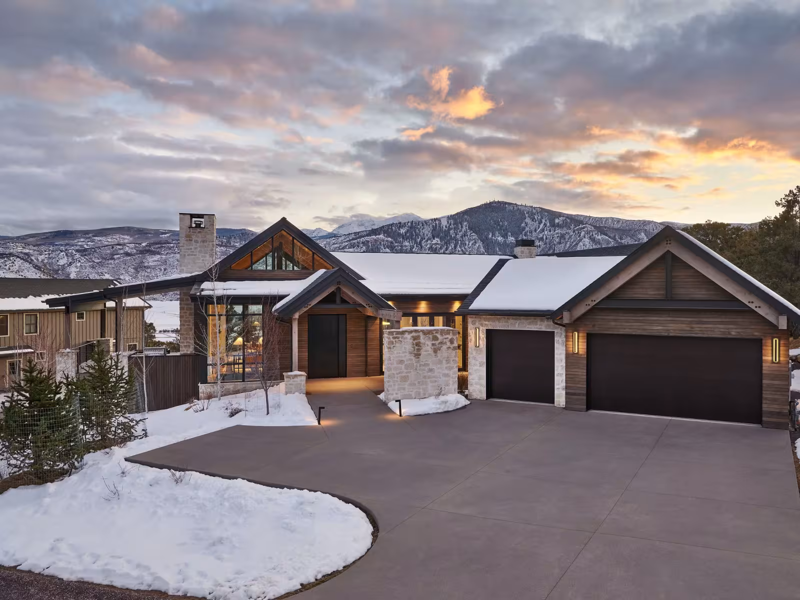 Snow-covered house with mountains at sunset.