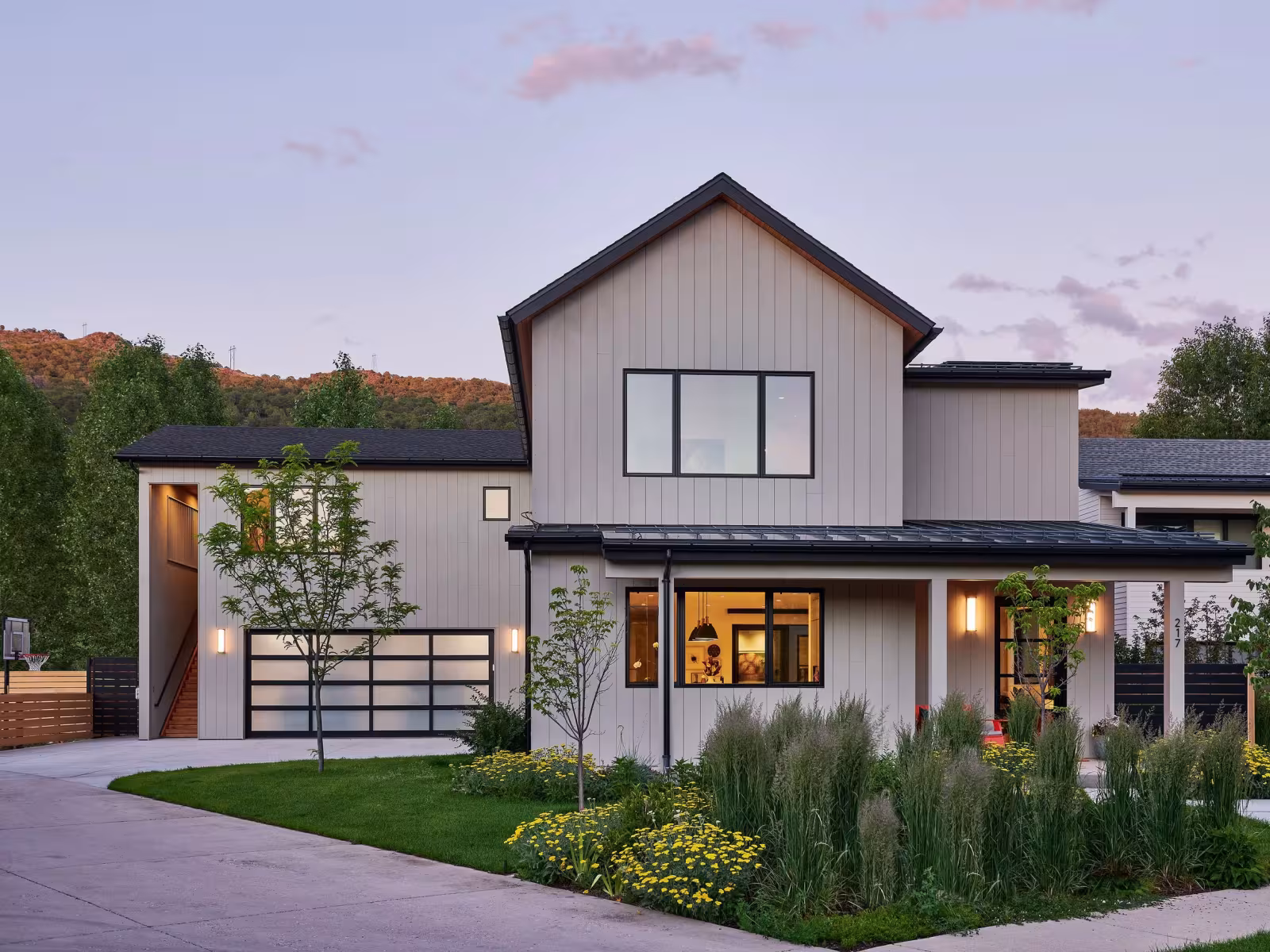 Modern house with large windows, surrounded by a garden at dusk.