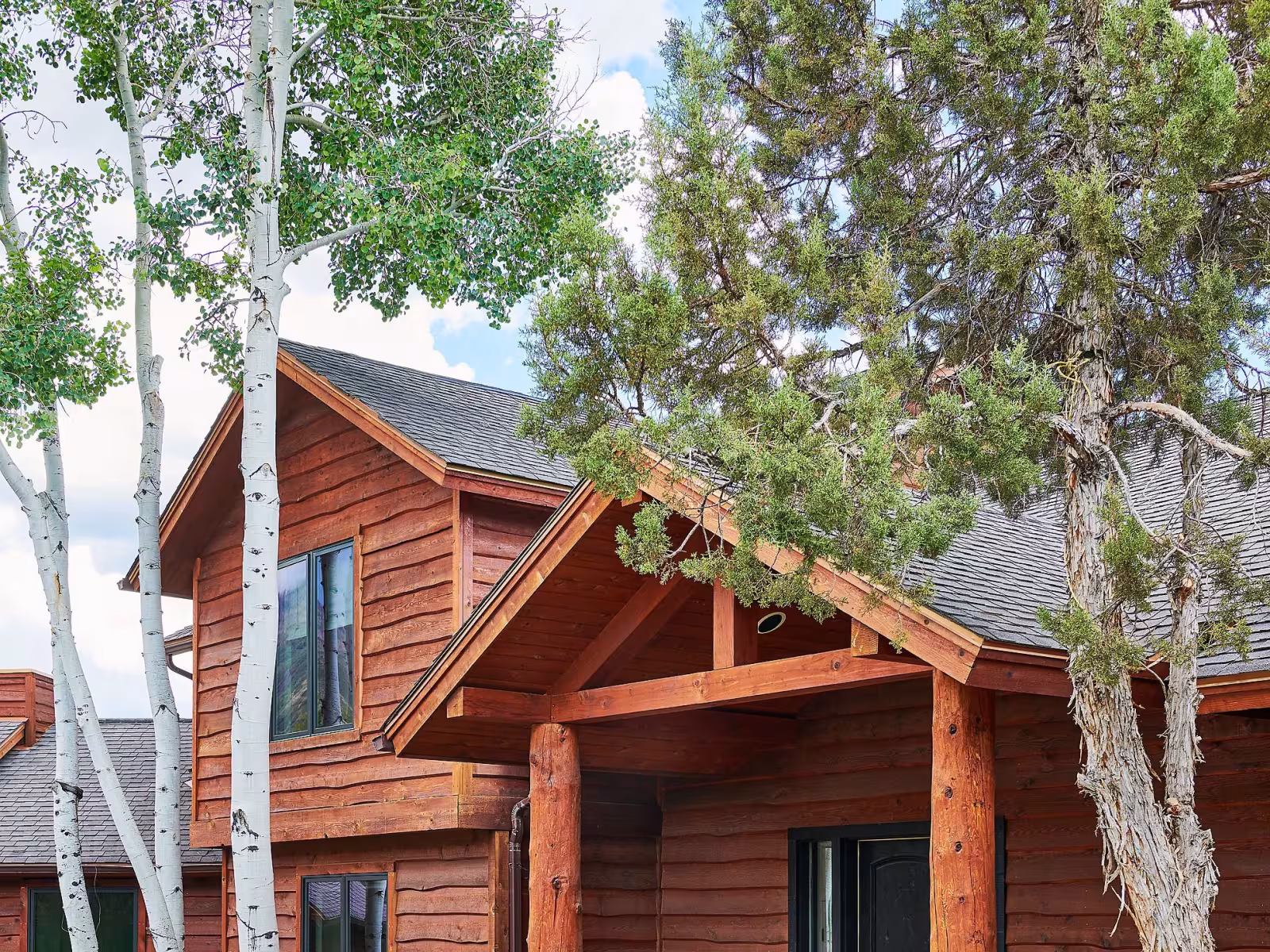 Rustic log cabin surrounded by trees and greenery on a sunny day.