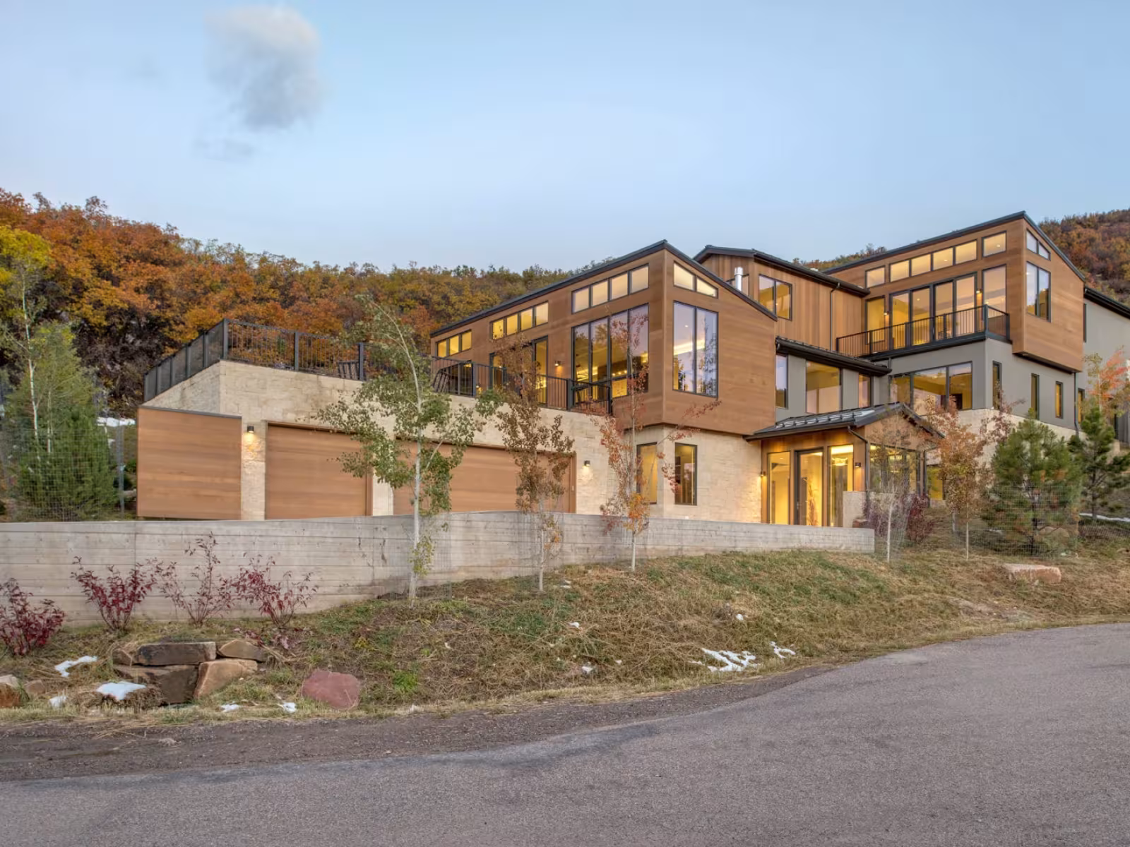 Modern wooden house with large windows, set against an autumn hillside.