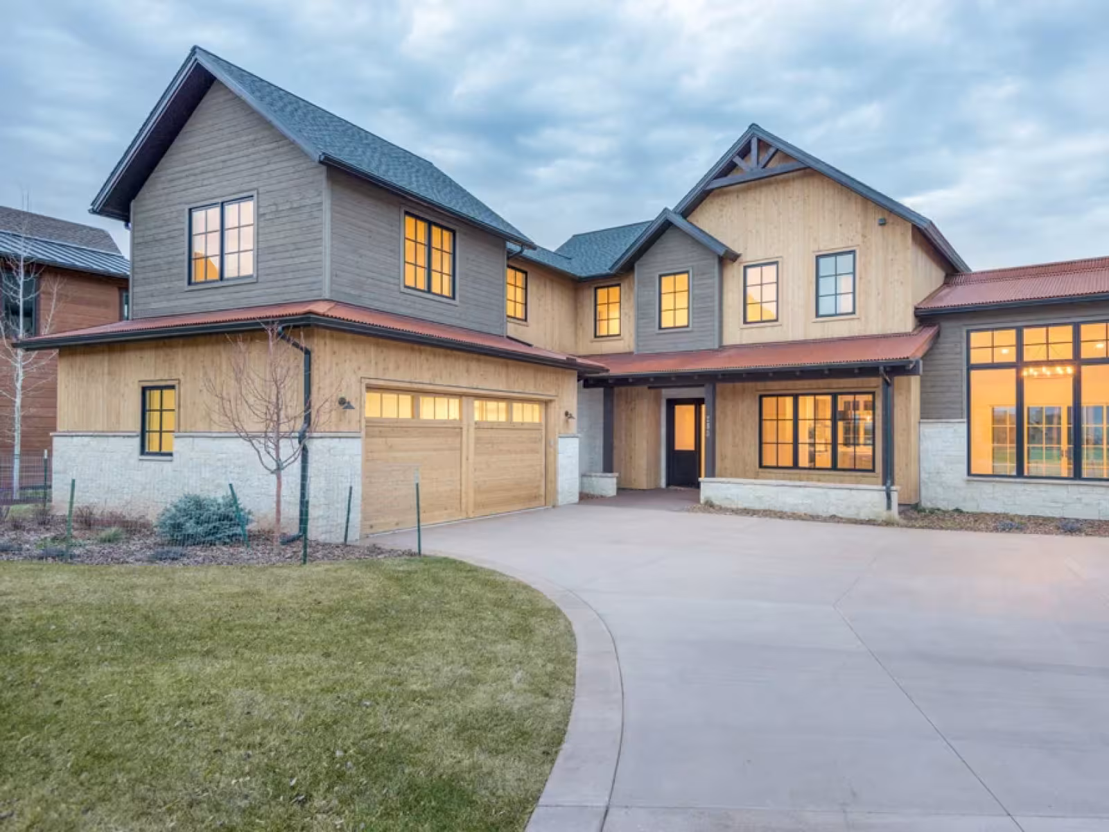 Large modern house with lit windows and a spacious driveway at dusk.