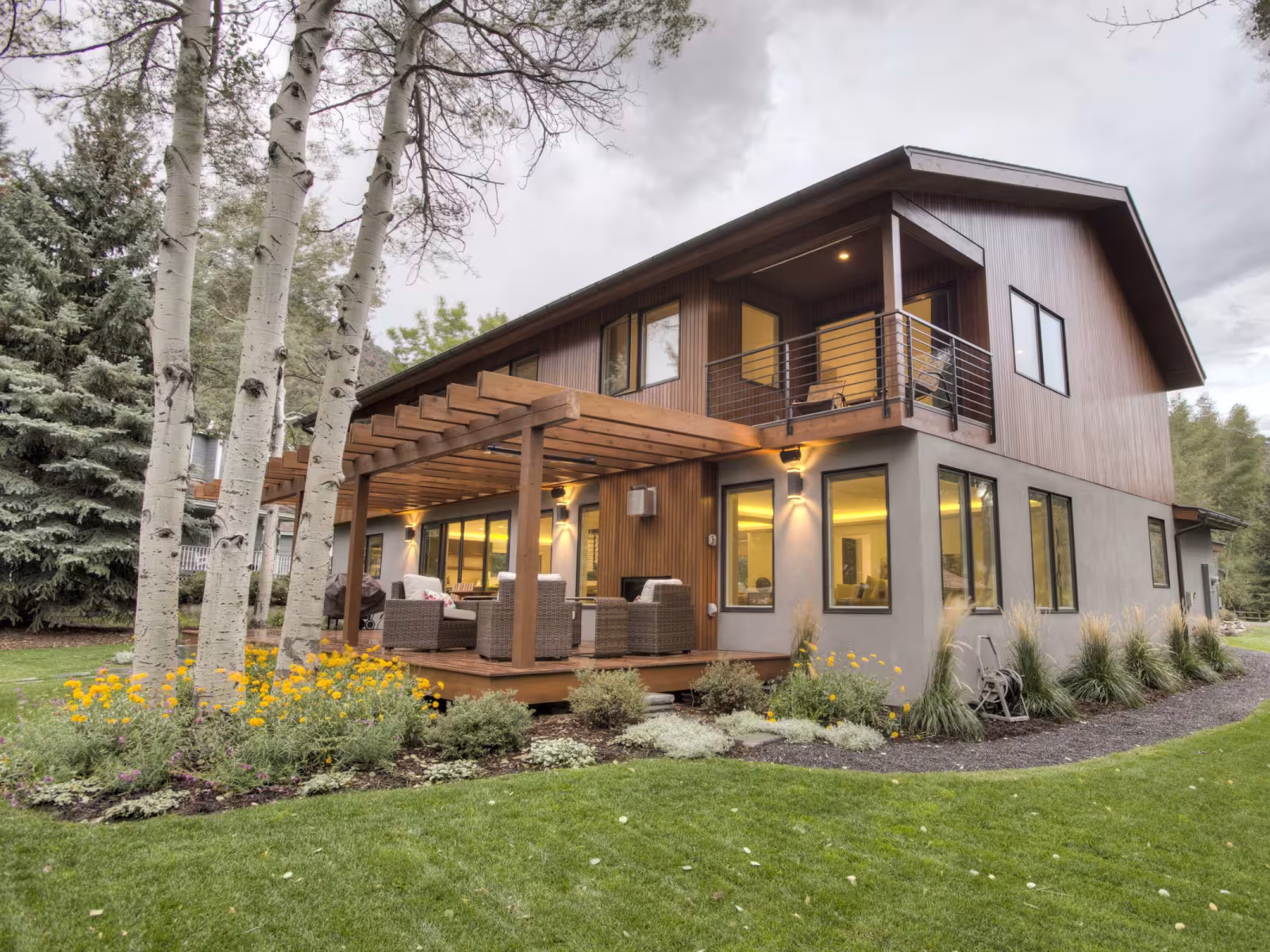 Modern two-storey house with wooden deck, set amidst trees and lawn.