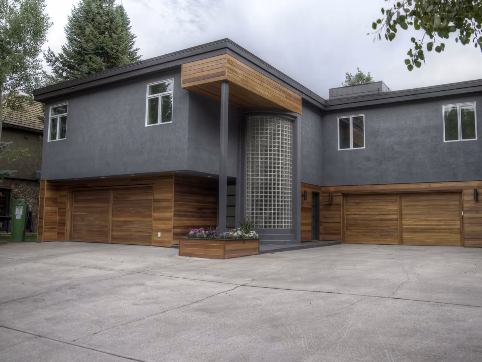 Modern grey and wood house with large windows and a spacious driveway.
