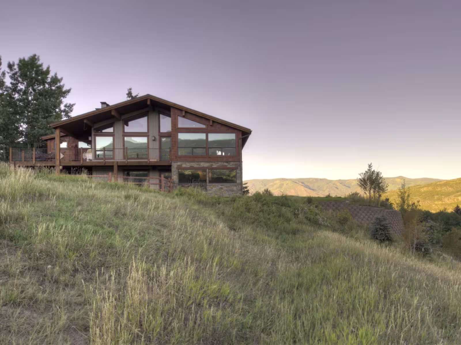 Wooden house on a grassy hill at sunset, overlooking distant mountains.