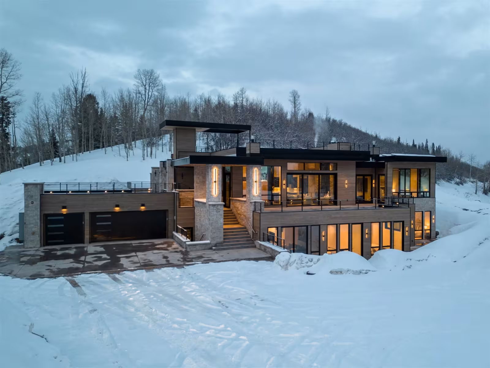 Modern house in snowy landscape, warm lights glowing inside.