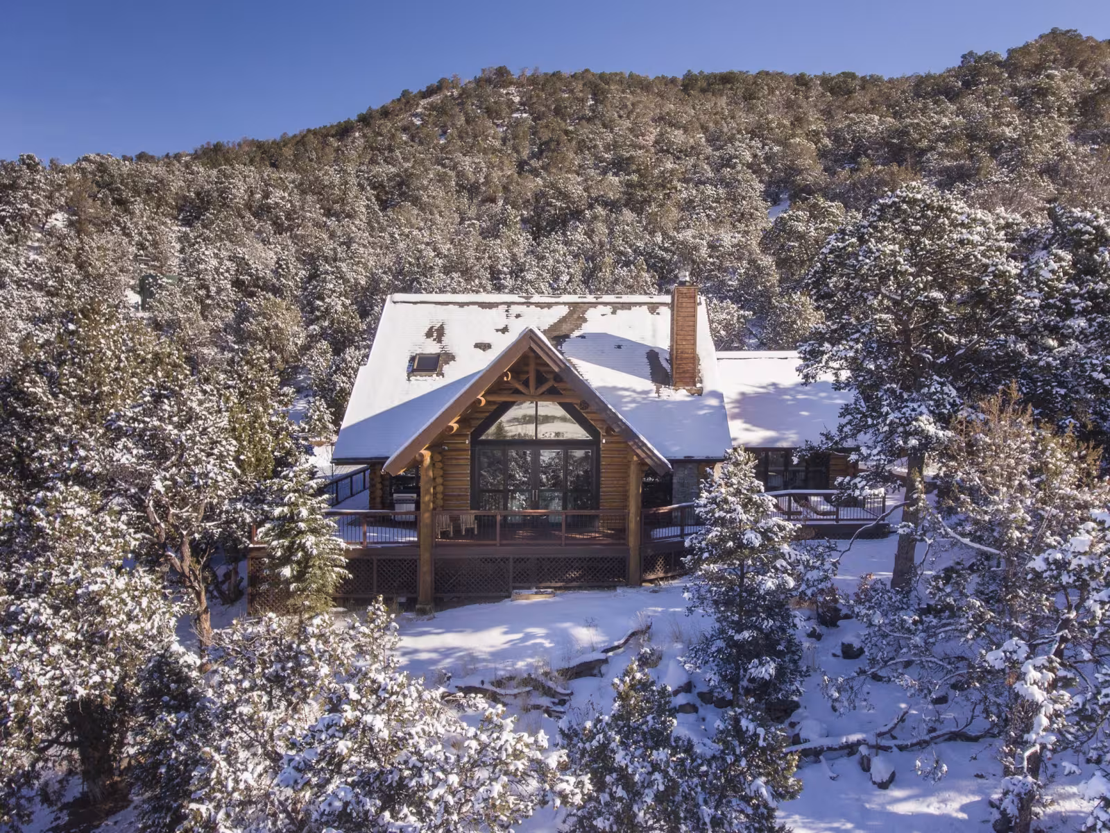 Mountain cabin surrounded by snow-covered trees under a clear blue sky.