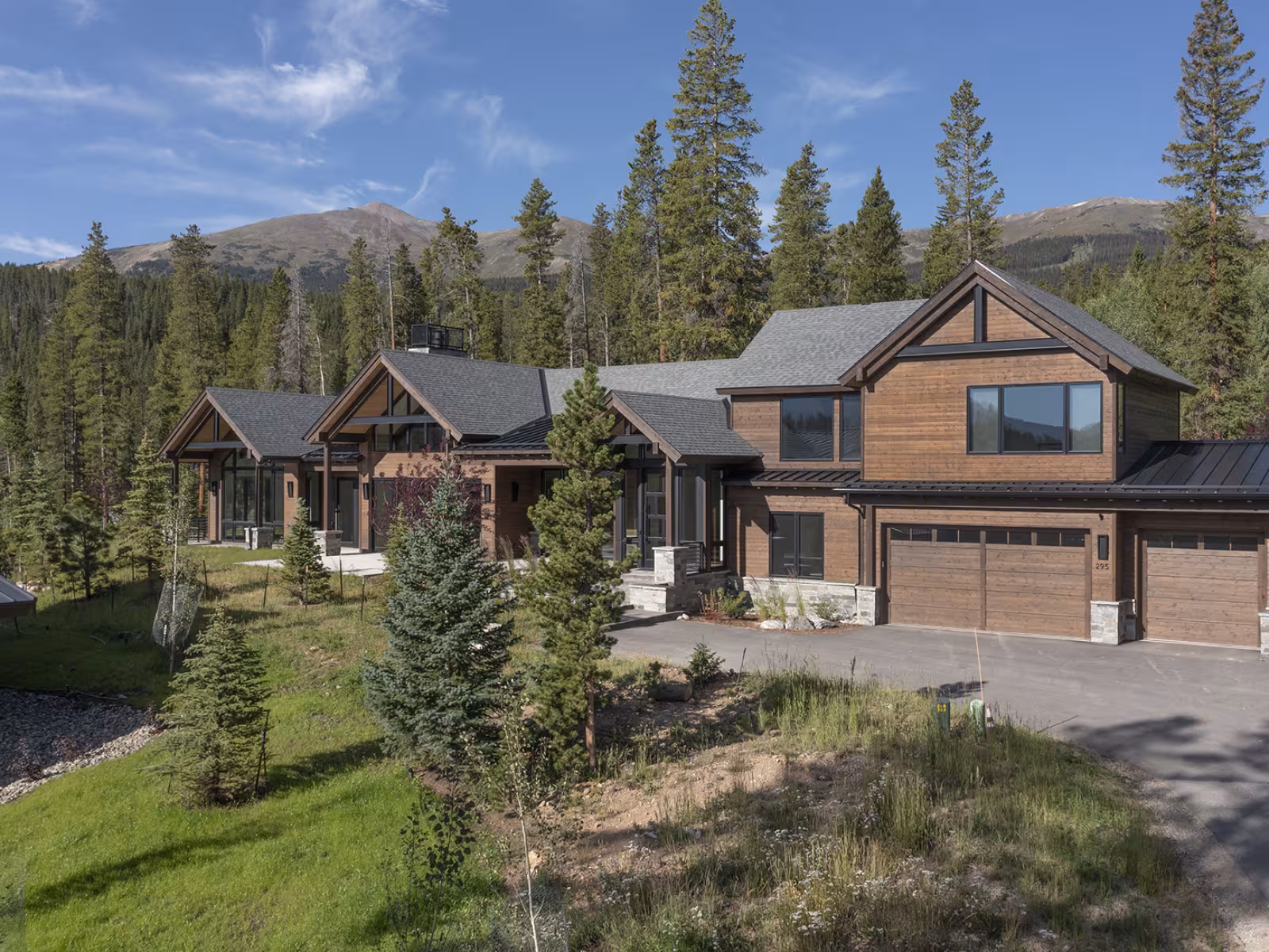 Spacious wooden house amidst tall pine trees and mountains.