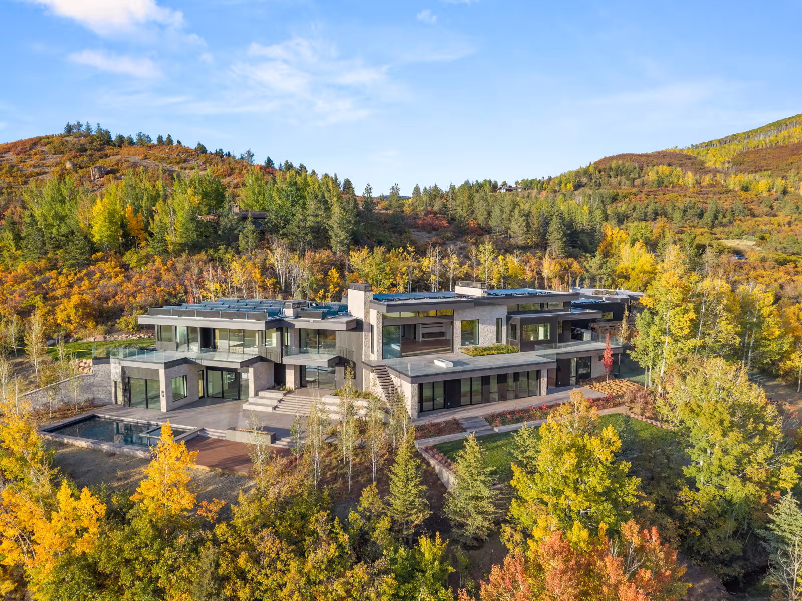Modern house surrounded by autumn trees, hillside backdrop.