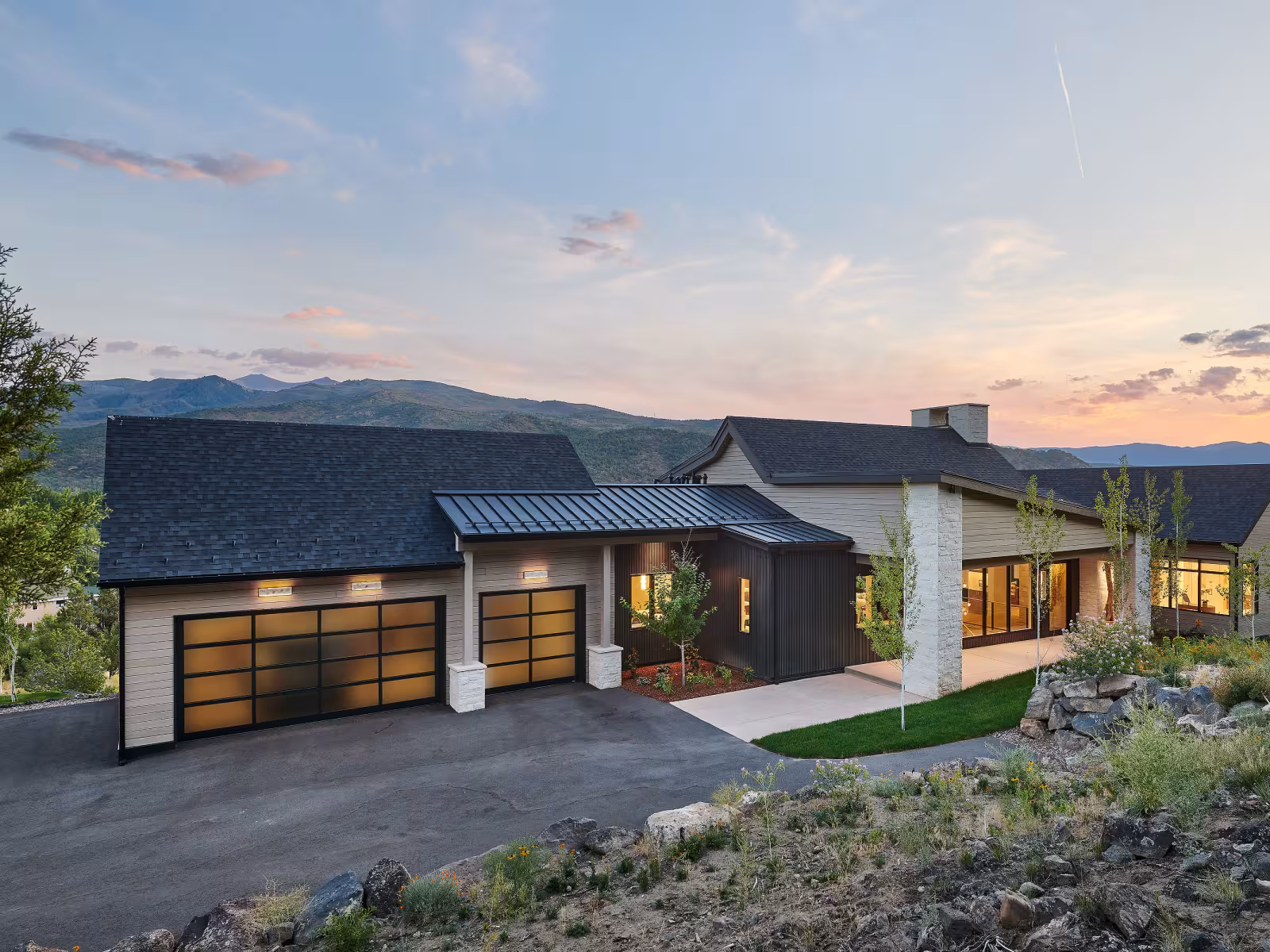 Modern house with large windows at sunset, surrounded by hills.